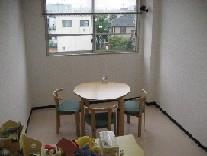 丸いテーブルを囲むように椅子があり、テーブルの奥の小窓からは住宅が見えている相談室の写真
