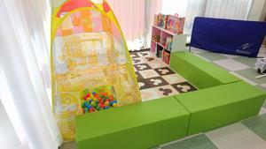 黄緑のソファーで仕切られたキッズスペースに本棚があり、カラーボールが入っている遊具がある写真