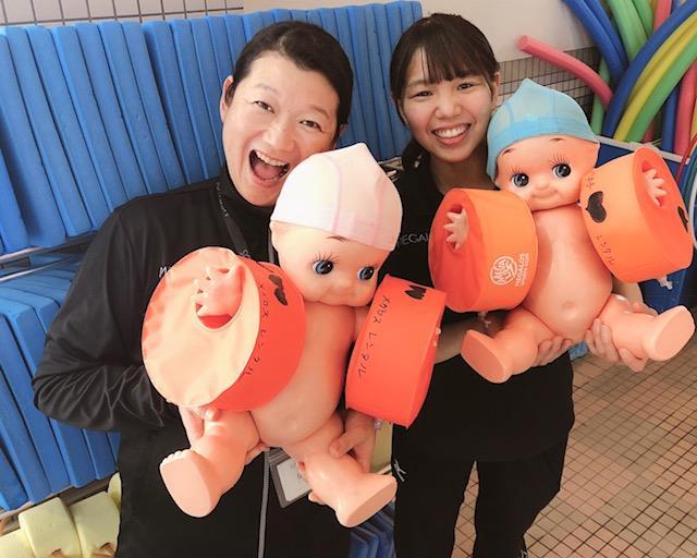 腕に浮き輪をした赤ちゃんの人形を抱えている女性2人の写真