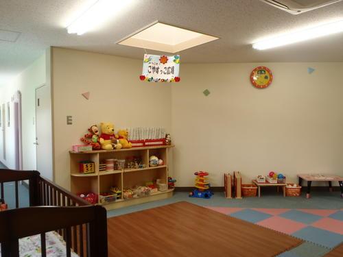 壁沿いにおもちゃや本棚が並び手前にベビーベット、中央はマットが敷かれている室内の写真
