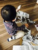 小さな男の子が新聞紙をちぎって遊んでいる写真