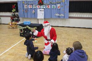 児童館のクリスマス会でサンタクロースからプレゼントをもらう幼児と保護者の写真